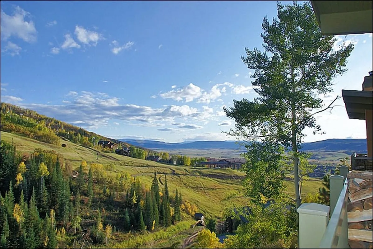 This image captures sweeping views of rolling hills and distant mountains under a bright blue sky. Lush greenery fills the foreground, and the expansive vista evokes a sense of tranquility and connection to the natural world.