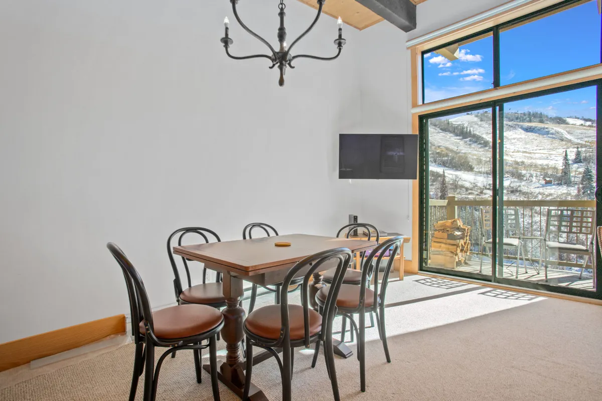 A spacious dining area featuring a large table set for six beneath elegant chandeliers, with wide windows framing sweeping mountain vistas. The scene is perfectly staged for family dinners, lively celebrations, or casual game nights, emphasizing social connection and the alpine landscape beyond.