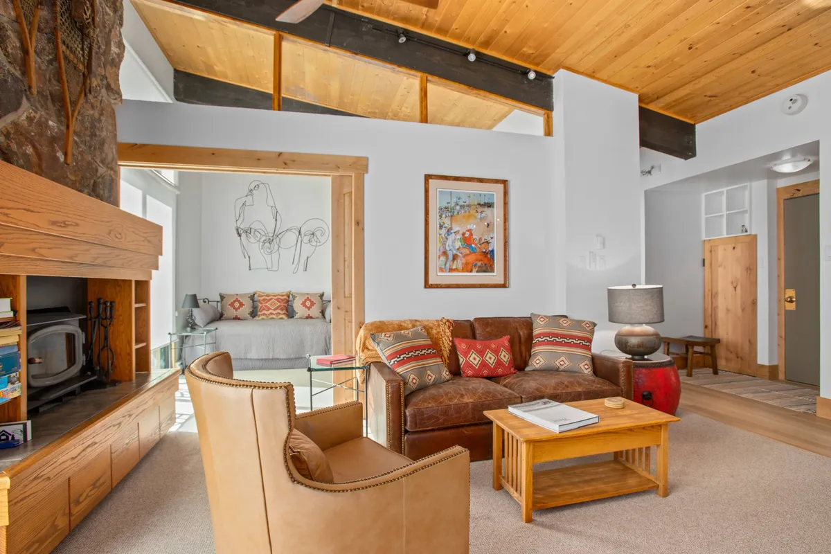 A stylish, cozy living room with a comfortable sofa, decorative pillows, a wooden coffee table, curated artwork, and a beautiful stone fireplace. Large windows (not pictured directly) are implied, offering a tranquil space for relaxation after a productive day.
