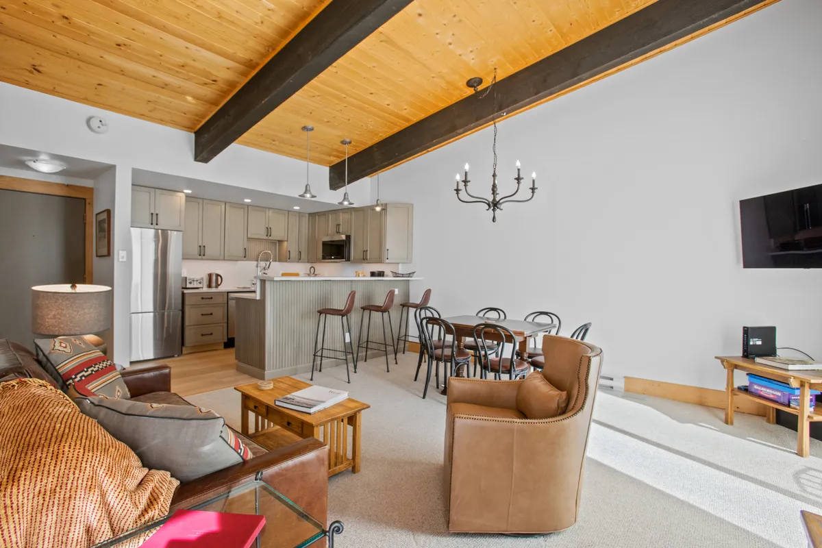 A spacious, comfortable open-plan living and dining area with a kitchen island, chandelier, sofa, dining table, and a television, all set within a warm, inviting atmosphere.