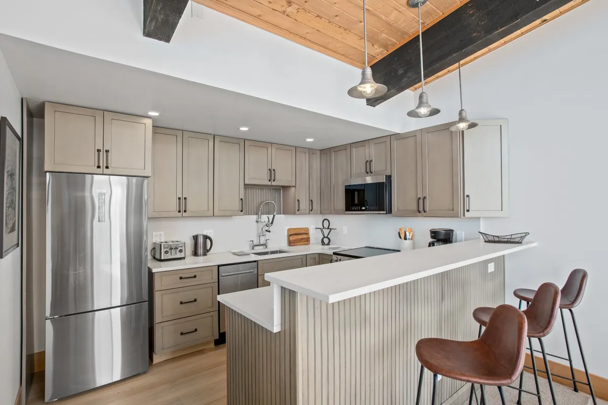 A modern kitchen with a large island, stainless steel appliances, warm wooden beams, and bar stools inviting guests to linger. The layout is open and welcoming—ideal for entertaining, preparing family meals, or enjoying a casual breakfast at the breakfast bar.
