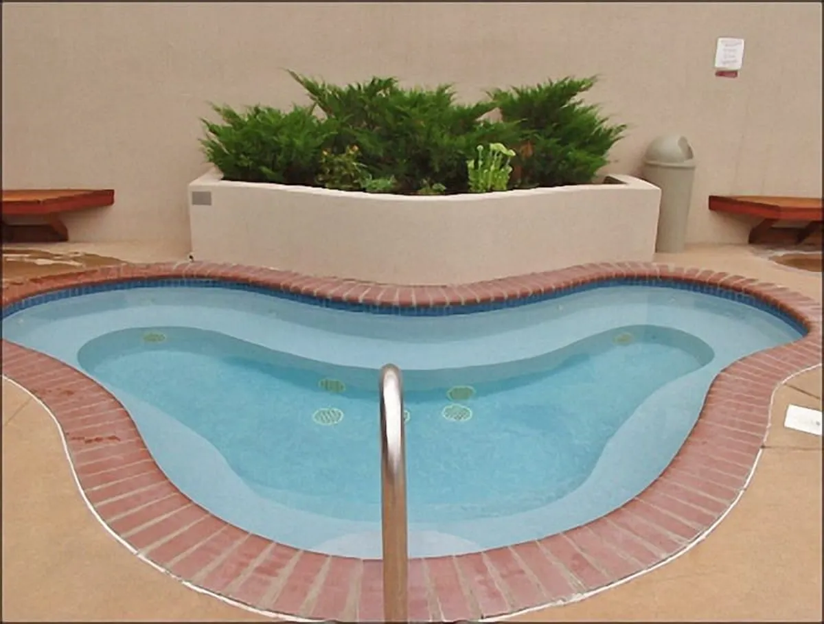 A tranquil outdoor heated swimming pool is surrounded by green plants and a brick edge, with the serene ambiance suggesting a perfect après-ski relaxation spot. Although not pictured in winter, the pool is visually inviting and hints at the available amenities for guests after a day on the mountain.
