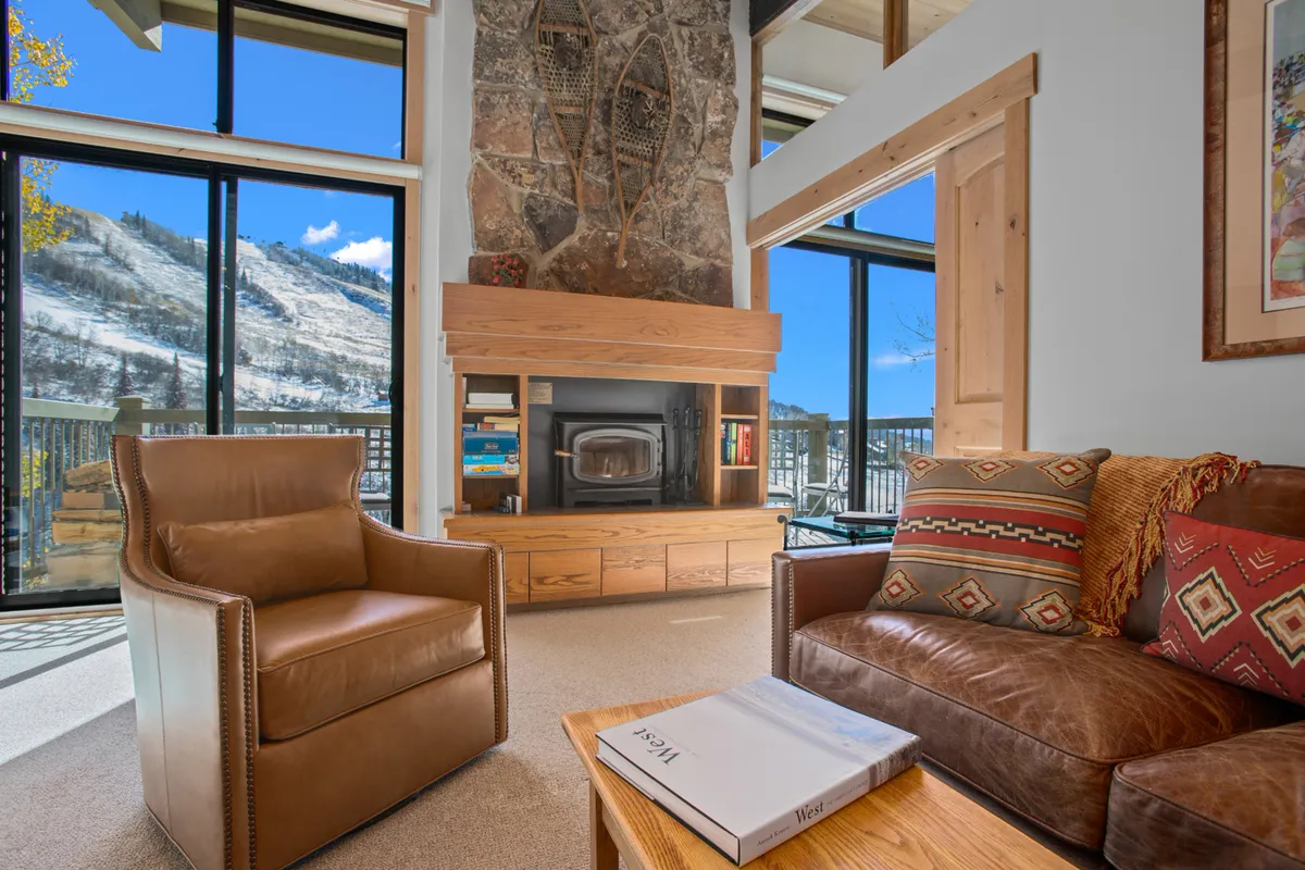 An inviting living area featuring a fireplace, large windows with breathtaking mountain views, and comfortable seating. Snow can be seen outside, reinforcing the mountain setting and direct visual connection to the slopes.
